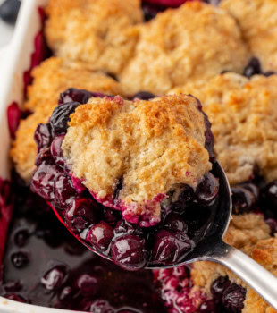 a spoonful of blueberry cobbler with remaining cobbler in the background