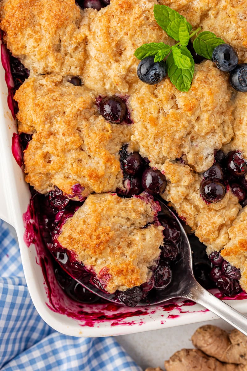 blueberry cobbler in a white baking dish with a spoonful of cobbler resting in the corner