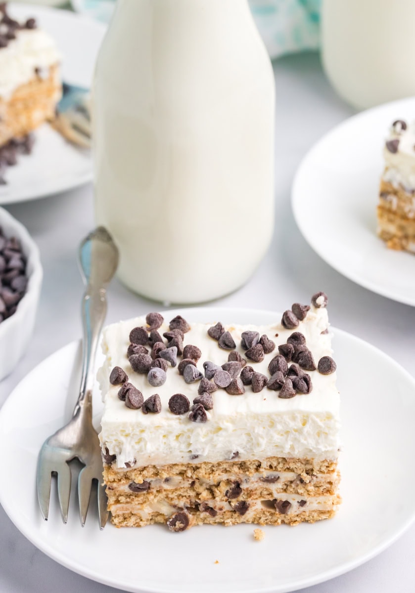 a slice of cannoli icebox cake on a white plate with more servings and a bottle of milk in the background