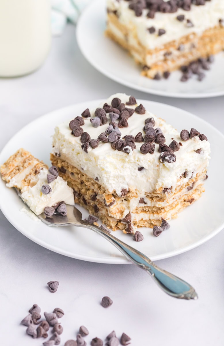 a slice of cannoli icebox cake on a white plate with a bite on a fork; another slice partially visible in the background