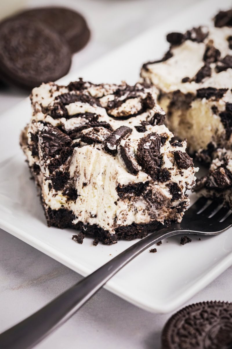 an Oreo cheesecake bar on a white plate with a bite on a fork