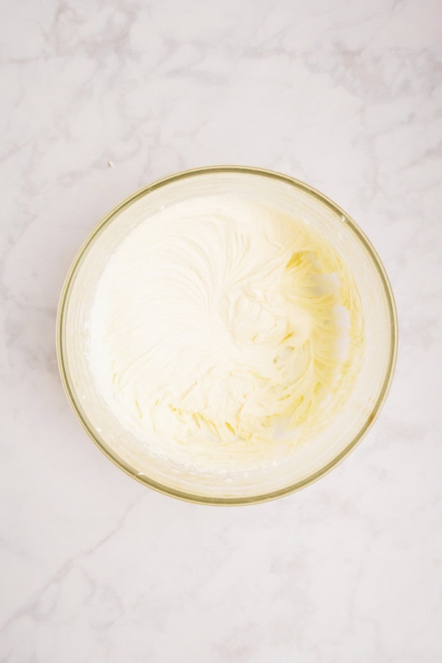 overhead view of mixed cream cheese, sugar, and vanilla in a glass mixing bowl