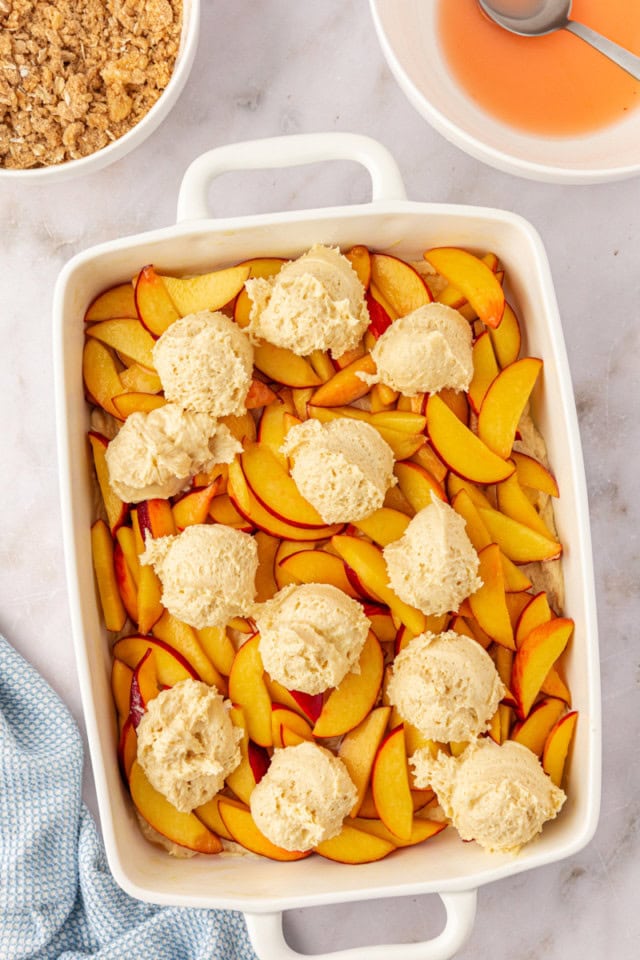 overhead view of cake batter dolloped on top of a layer of peaches for peach coffee cake