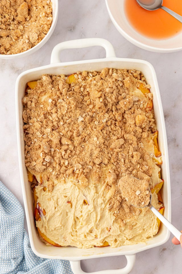 overhead view of crumb topping being sprinkled over peach coffee cake