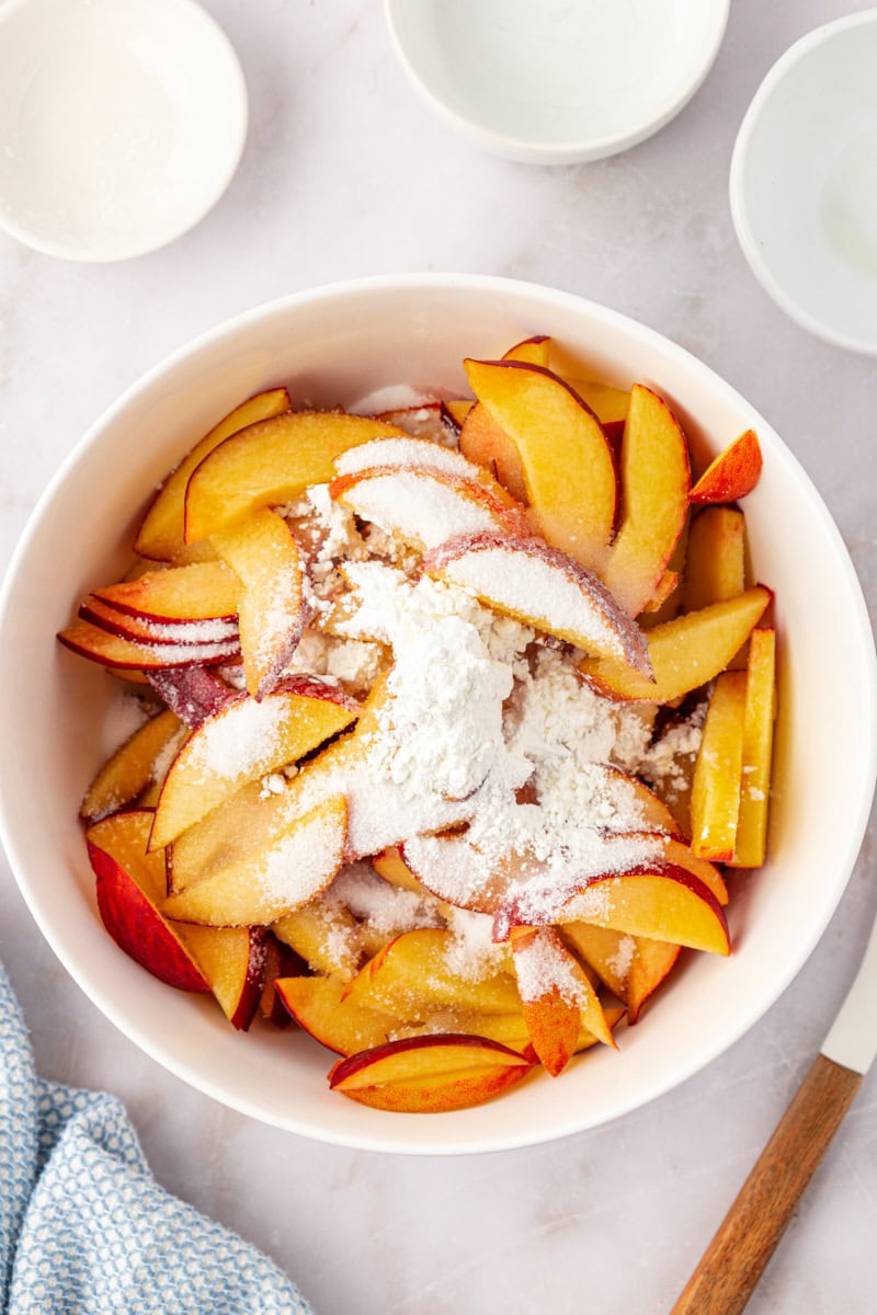 overhead view of peaches, sugar, lemon juice, and cornstarch in a white mixing bowl