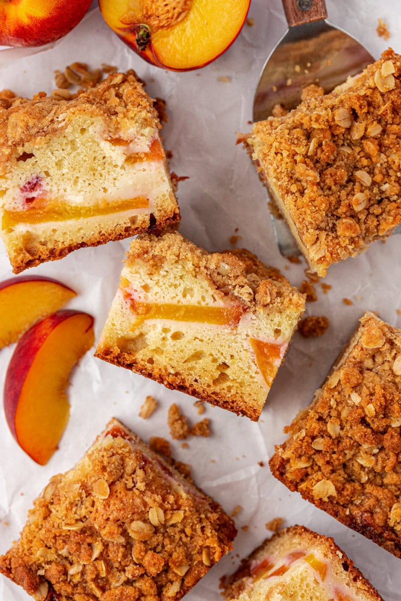 overhead view of slices of peach coffee cake and sliced peaches on a white surface