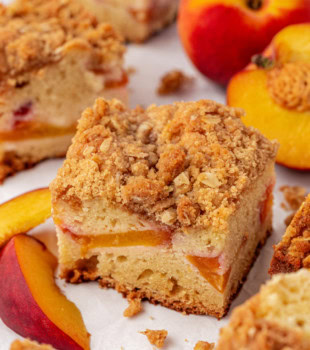 a slice of peach coffee cake surrounded by more cake and fresh peaches