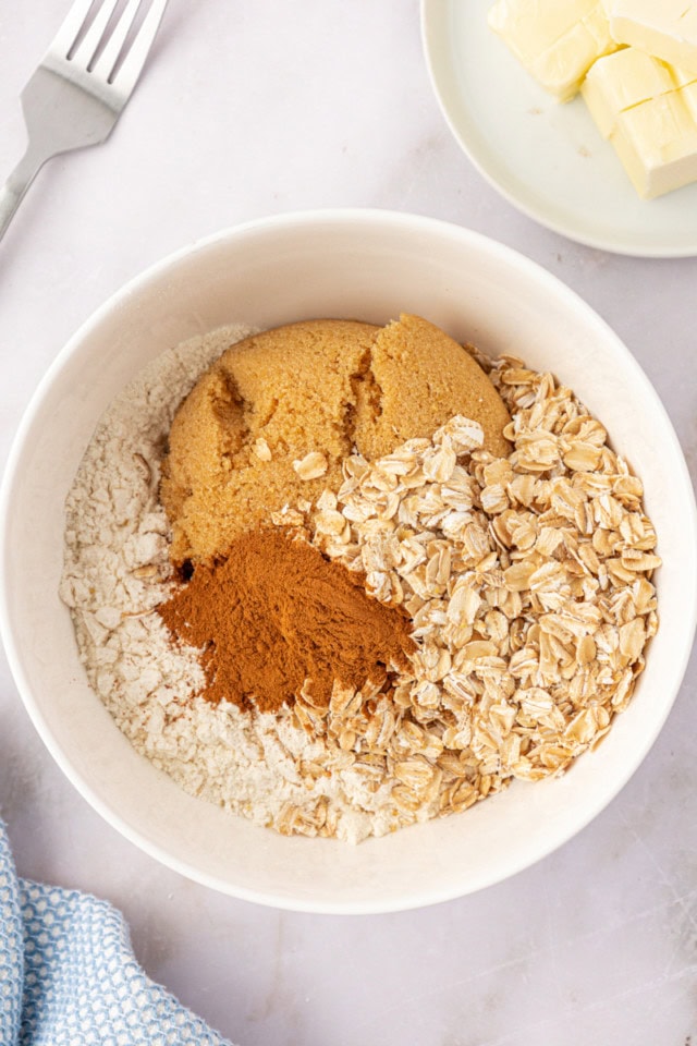 overhead view of flour, brown sugar, oats, and cinnamon in a white mixing bowl