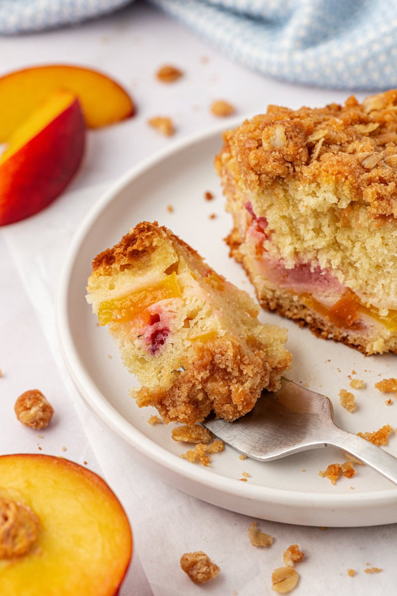 a bite of peach coffee cake on a fork resting on a plate with the remaining cake