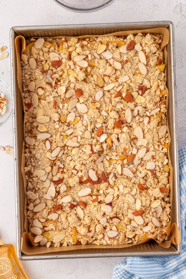 crumb topping and sliced almonds sprinkled over peach bars in a rectangular pan