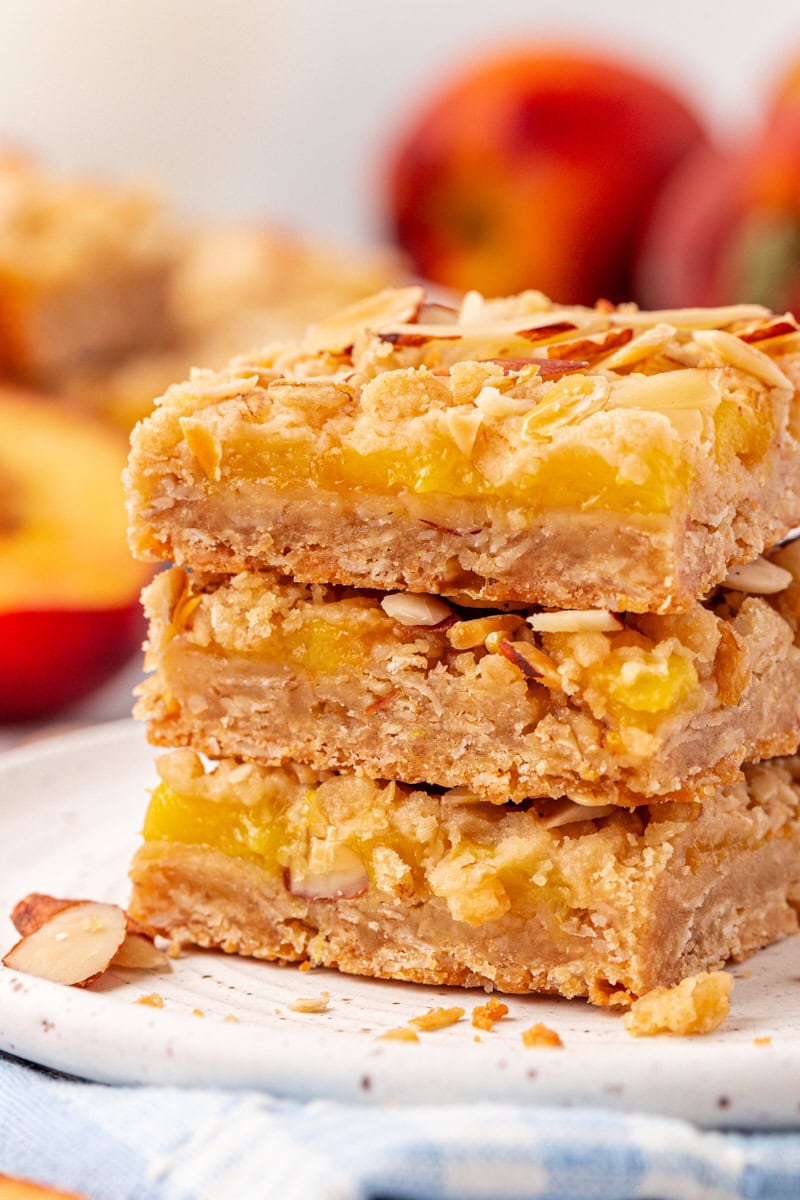 stack of three peach bars with more bars and fresh peaches in the background