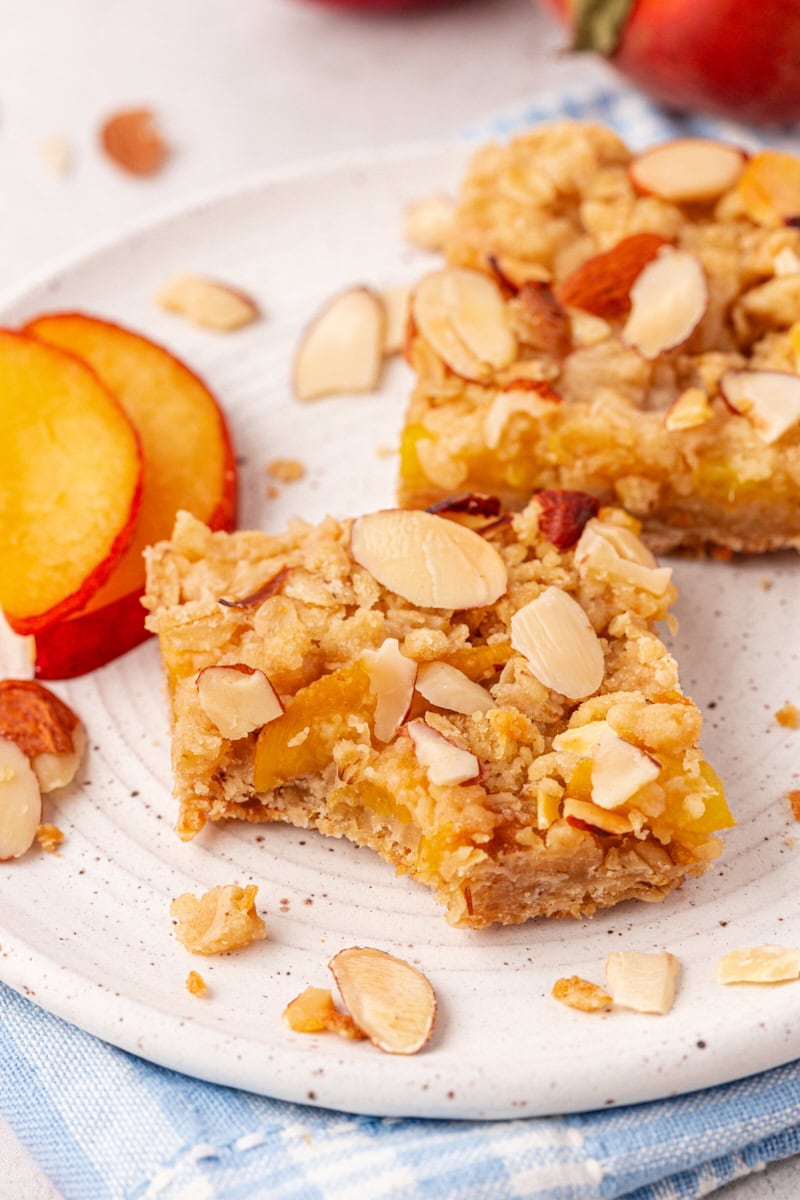 two peach bars on a white plate with a bite missing from one of them