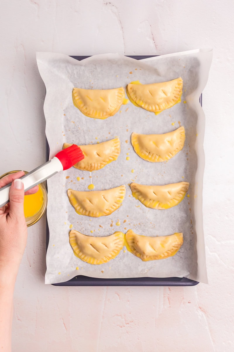 peach hand pies being brushed with egg wash on a baking sheet before going into the oven
