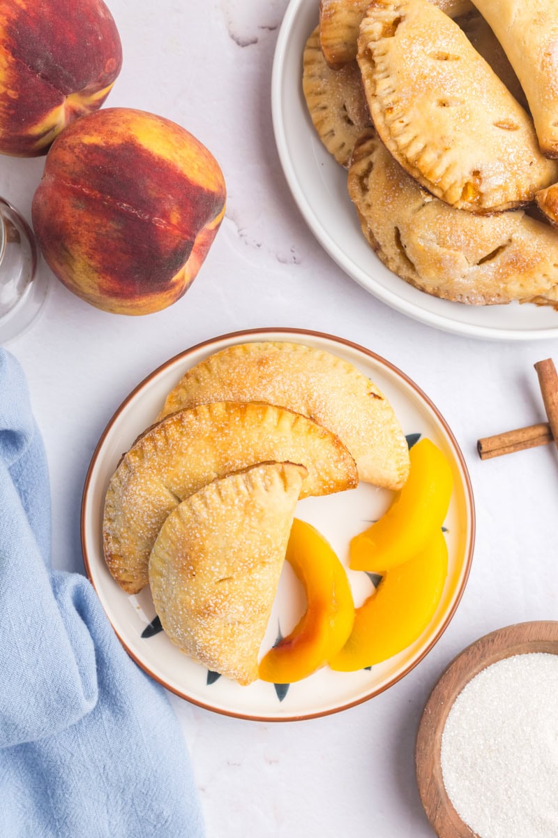 overhead view of three peach hand pies and peach slices on a white plate
