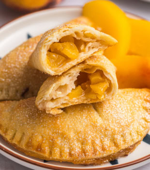 a peach hand pie cut in half, resting on top of two more pies on a plate