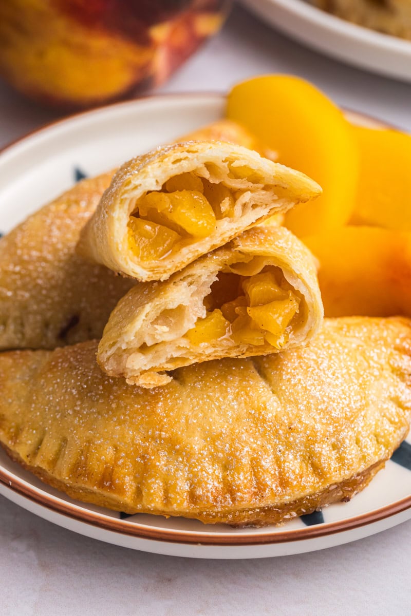 a peach hand pie cut in half, resting on top of two more pies on a plate