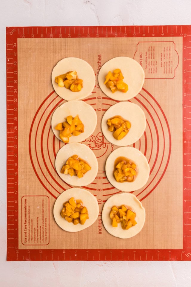 overhead view of peach hand pies being assembled on a silicone rolling mat