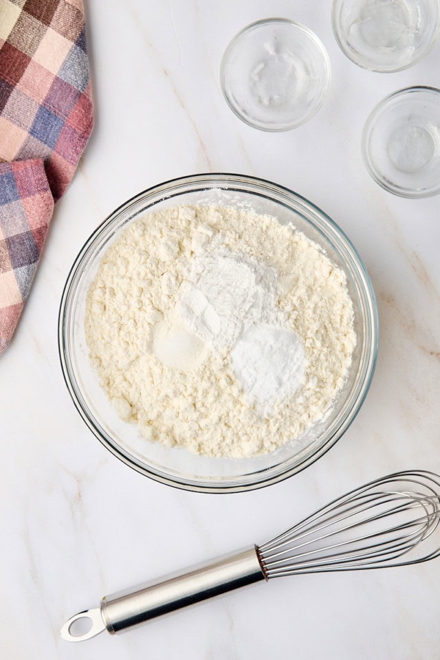 overhead view of flour, baking powder, baking soda, and salt in a glass mixing bowl