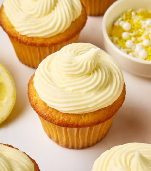 frosted lemon cupcakes on a white countertop with a bowl of white and yellow sprinkles partially visible