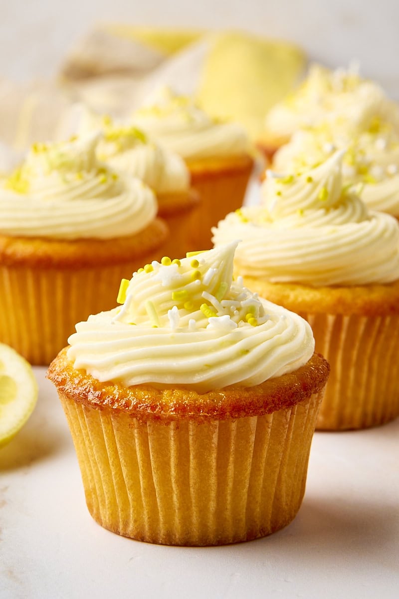 a lemon cupcake on a white surface with more cupcakes in the background