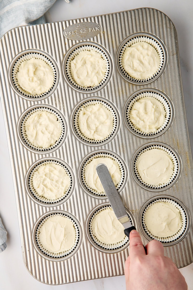 overhead view of no-bake cheesecake filling being spread on top of graham cracker crusts in a muffin pan