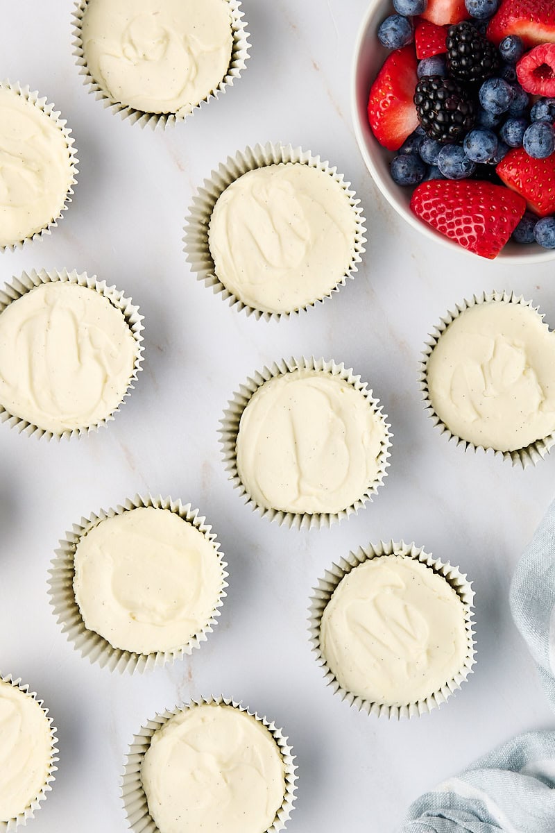 overhead view of mini no-bake cheesecakes and a bowl of fresh berries on a marble countertop