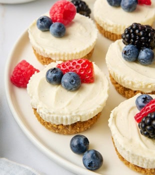 several mini no-bake cheesecakes served with fresh berries on a white plate