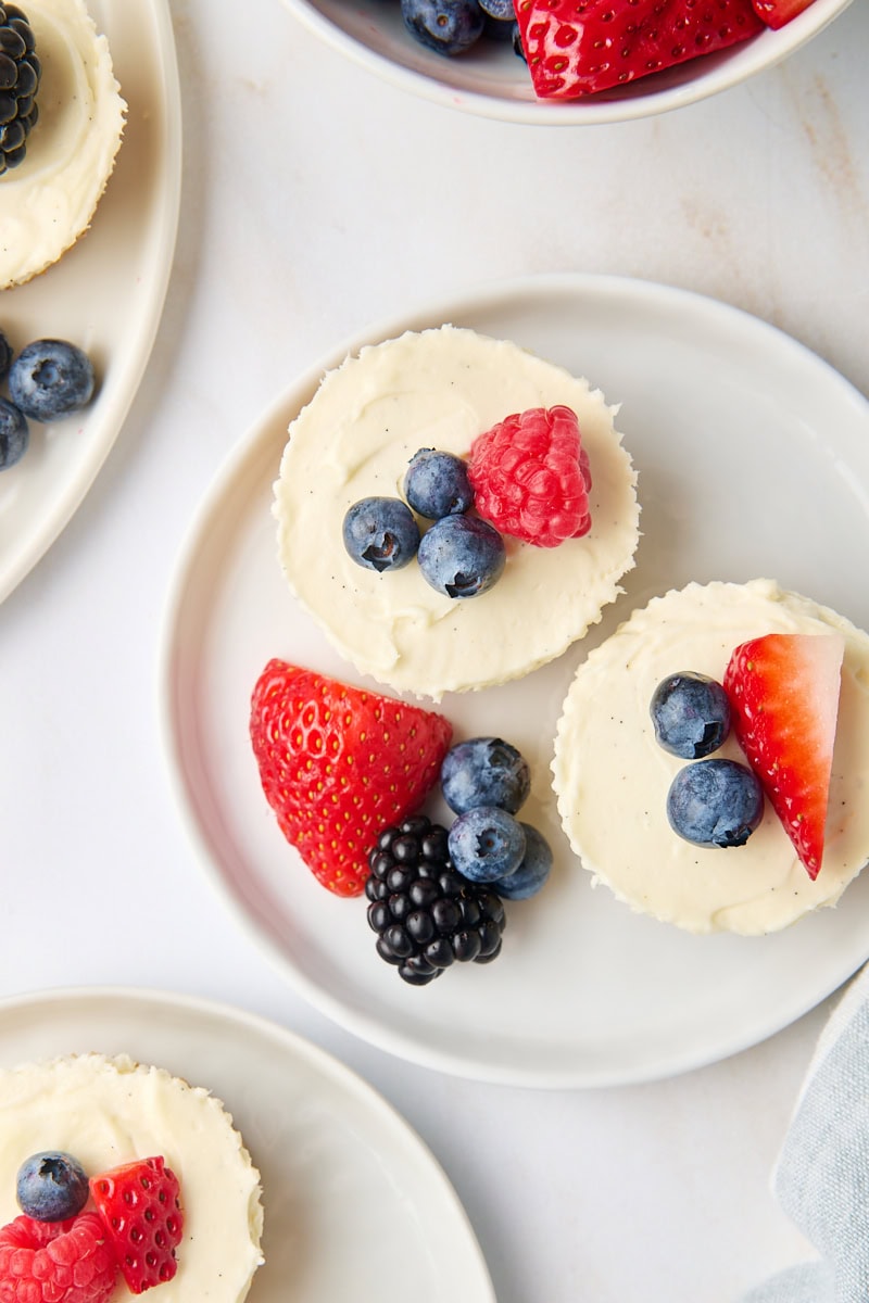 overhead view of mini no-bake cheesecakes topped with fresh berries on white plates