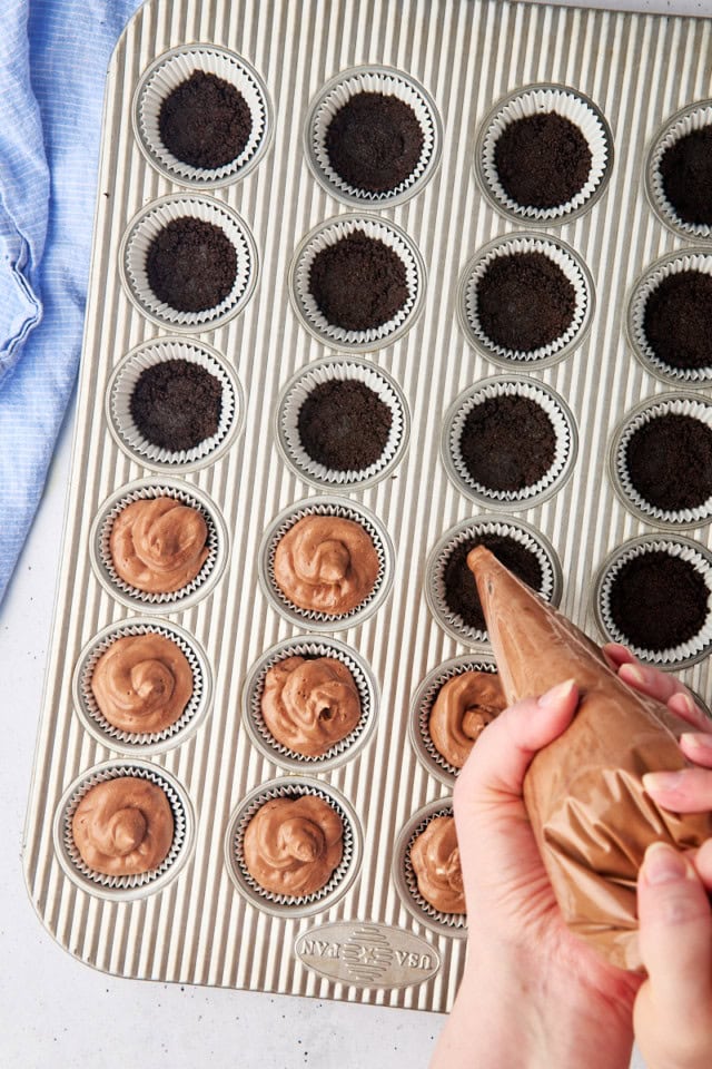 overhead view of no-bake chocolate cheesecake filling being piped onto Oreo crusts in a mini muffin pan