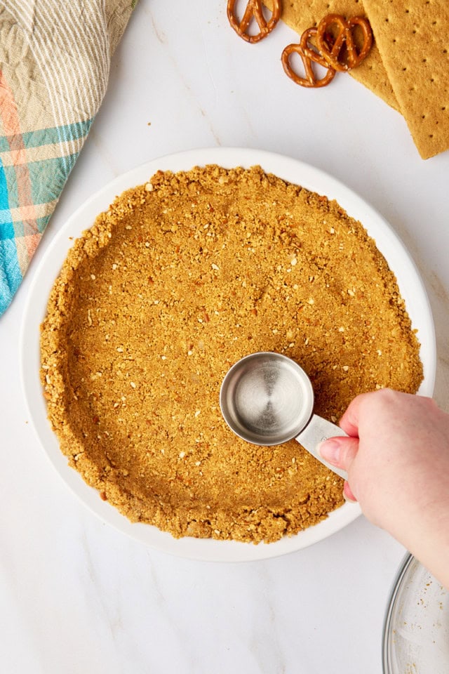 overhead view of graham-pretzel crust being pressed into a pie plate