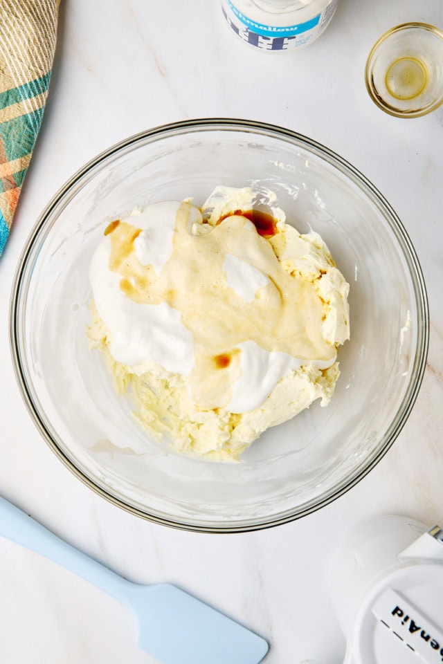 overhead view of marshmallow creme and vanilla extract added to beaten cream cheese in a glass mixing bowl