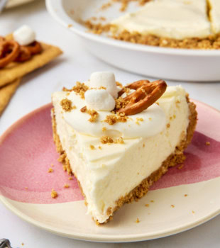 a slice of no-bake marshmallow cheesecake on a plate with remaining cheesecake in the background