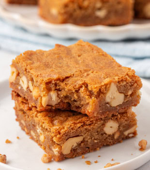 two brown butter blondies stacked on a white plate with a bite missing from the top bar