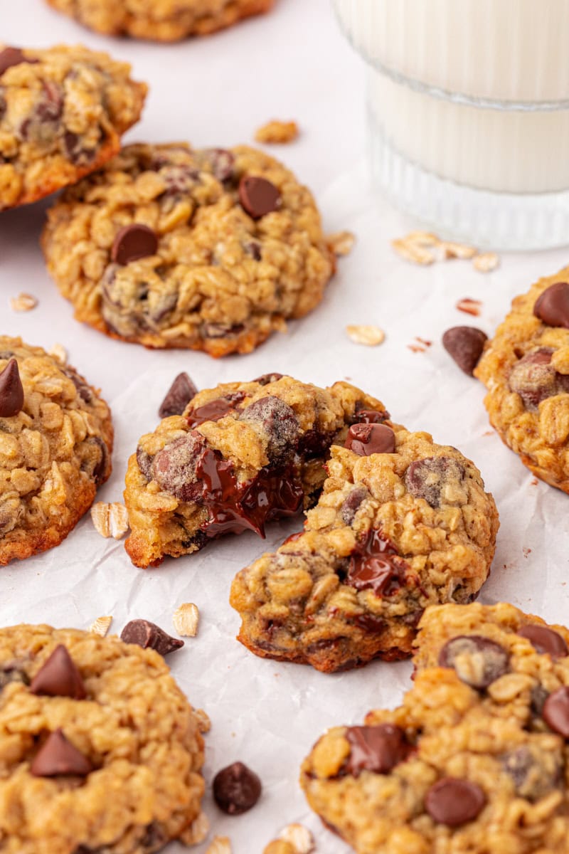 several brown sugar oatmeal chocolate chip cookies on a white surface with a glass of milk partially visible in the background