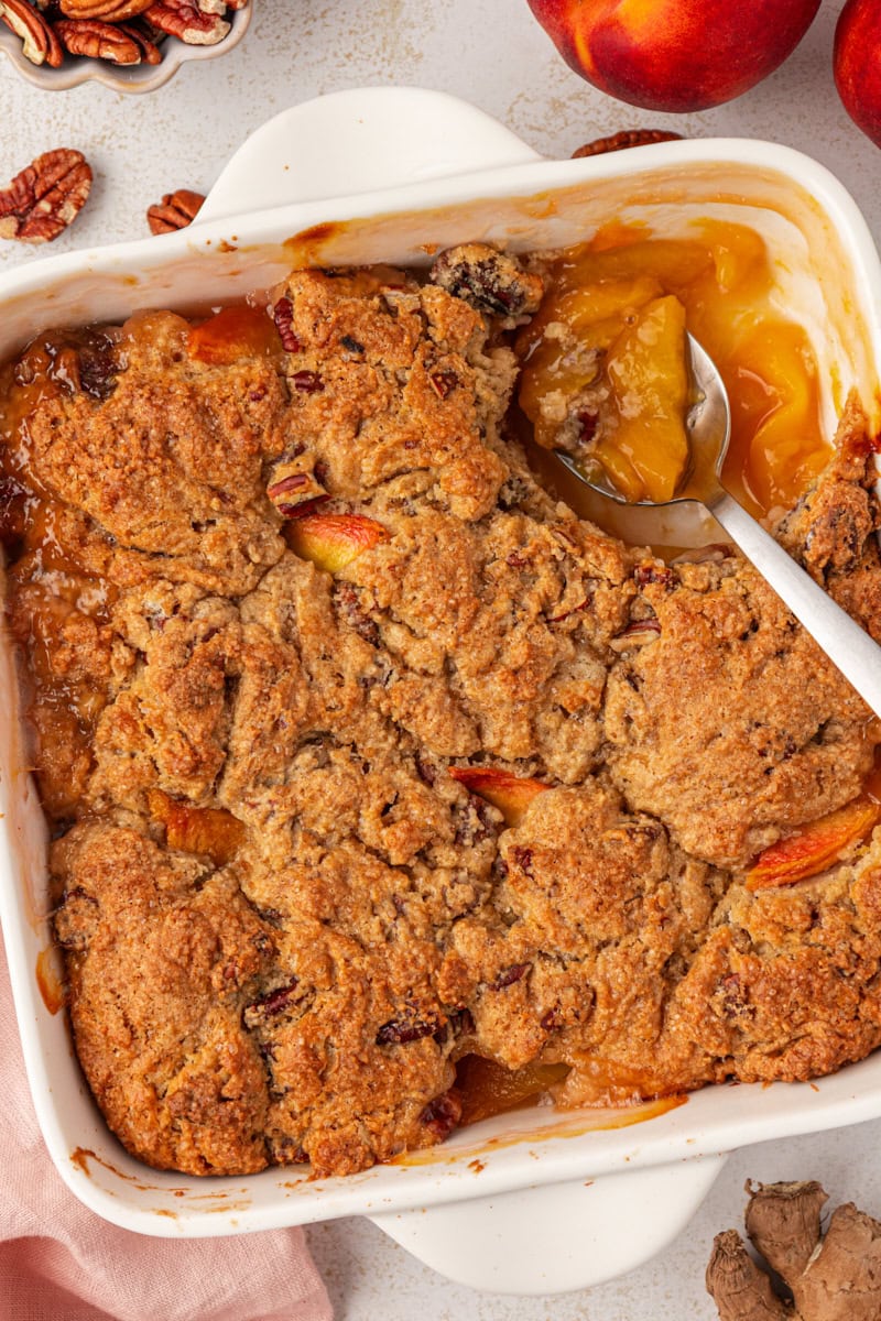 ginger peach cobbler in a white baking dish with a spoon resting in the corner where a portion is missing