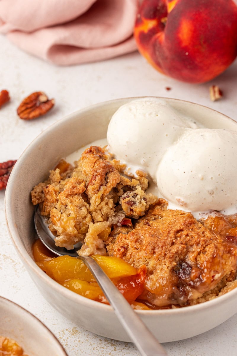 ginger peach cobbler topped with ice cream in a bowl with a spoon resting inside