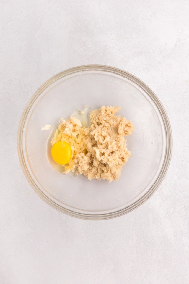 overhead view of egg added to creamed butter and sugar in a glass mixing bowl