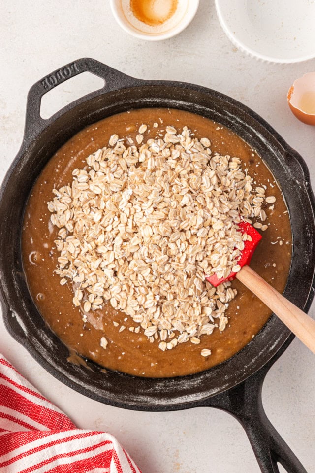 overhead view of oats added to cookie dough in a cast iron skillet