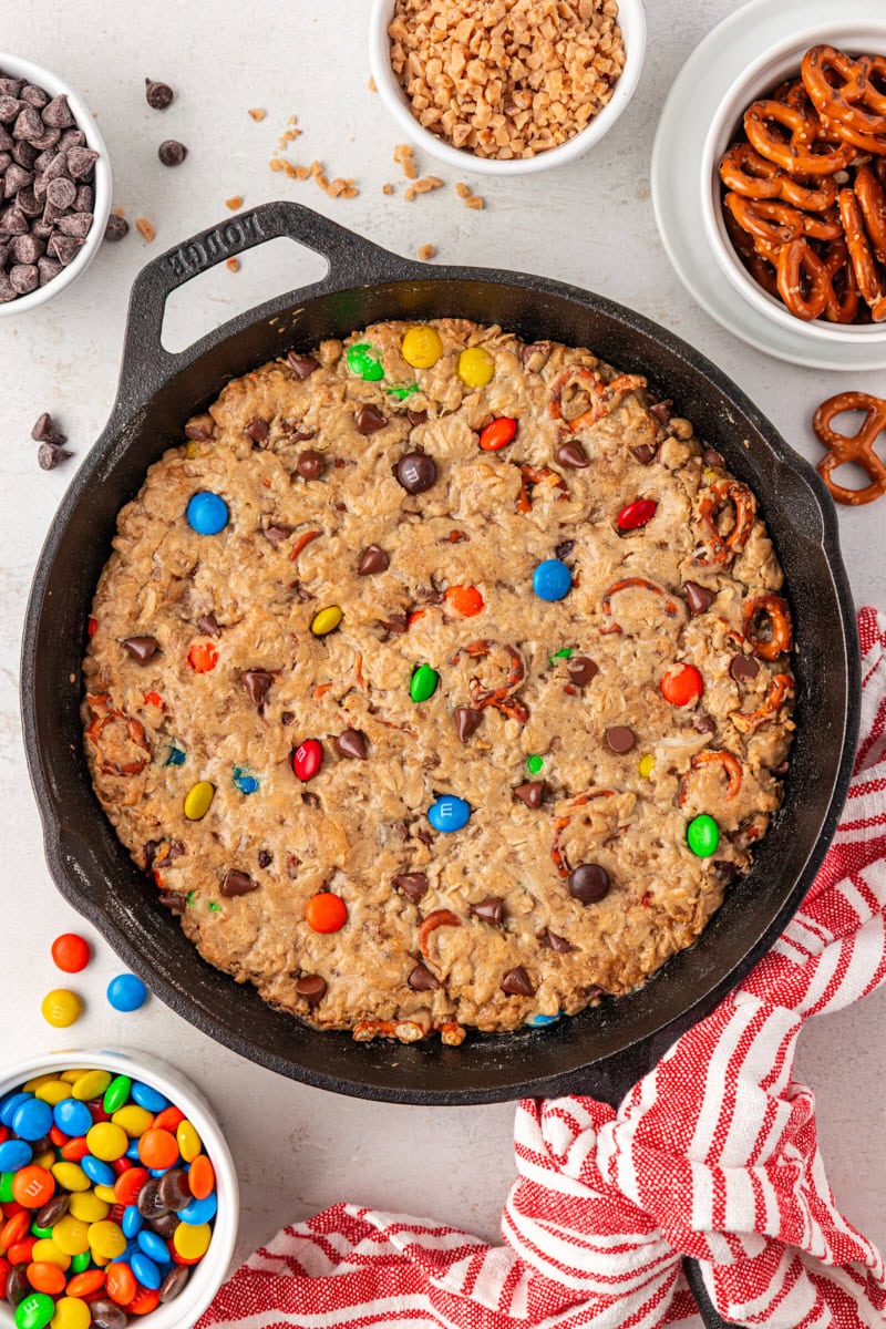 overhead view of monster skillet cookie on a white surface with small bowls of various add-ins surrounding