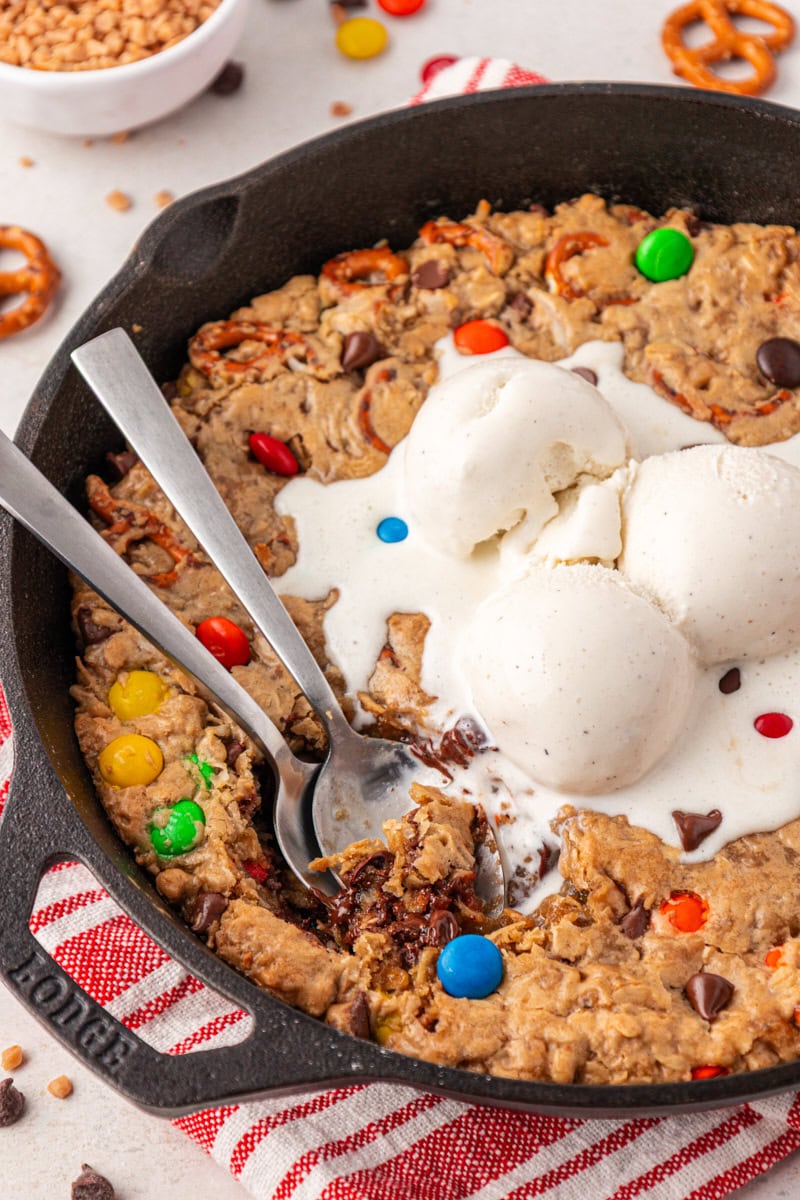 two spoons resting inside a skillet of monster skillet cookie topped with ice cream