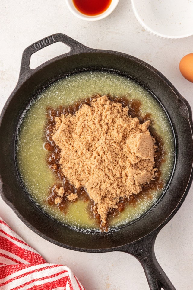 overhead view of brown sugar added to melted butter in a cast iron skillet