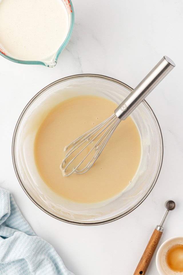overhead view of condensed milk, vanilla, and salt mixed together in a glass mixing bowl