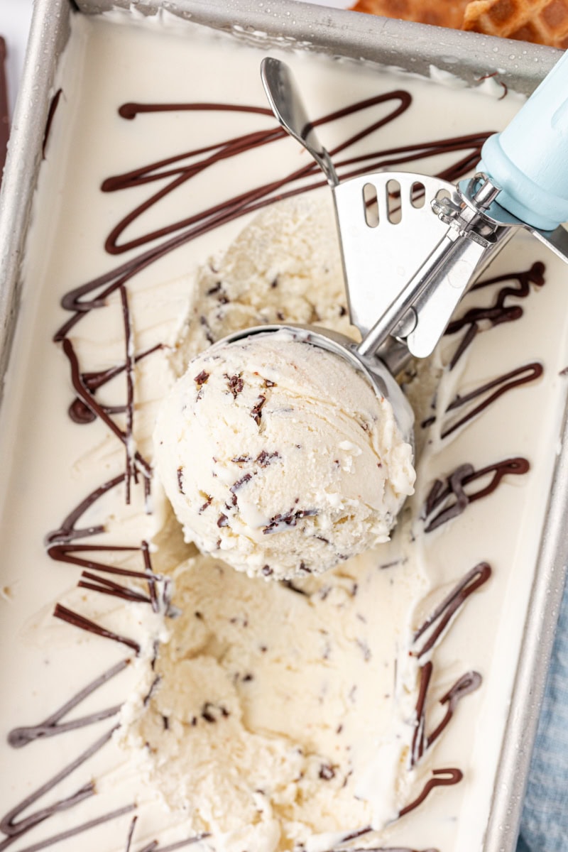 overhead view of stracciatella ice cream in an ice cream scoop resting on the remaining ice cream