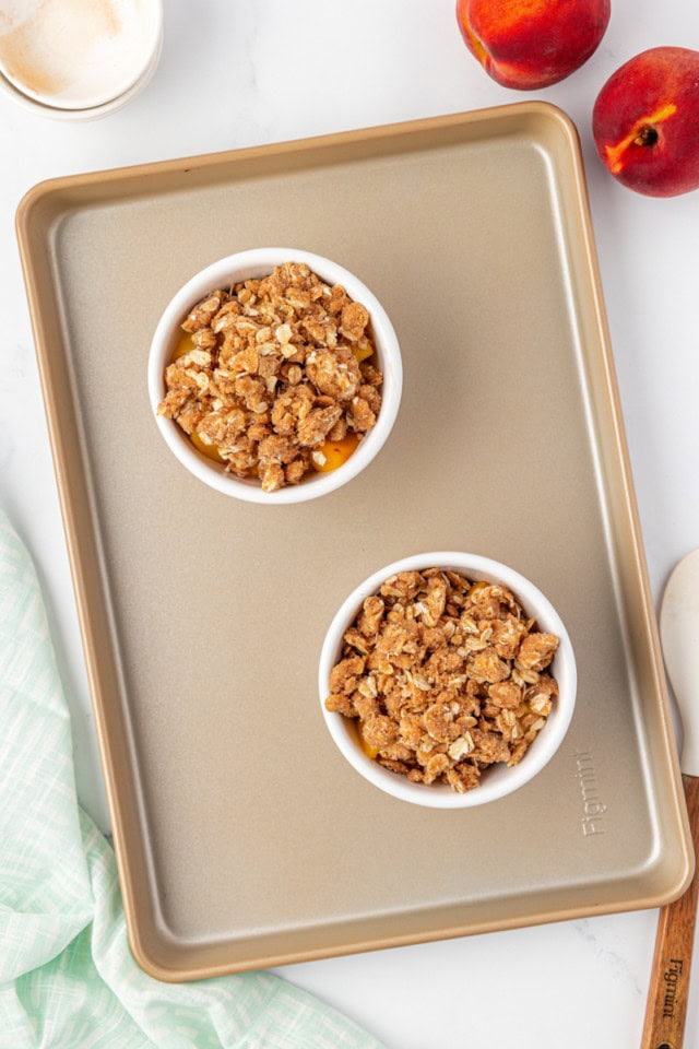 overhead view of peach crisp in two small bakers on a baking sheet