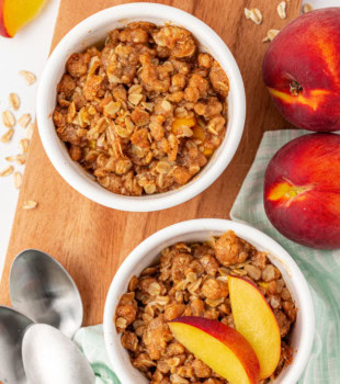 overhead view of peach crisp for two in white ramekins on a wooden cutting board