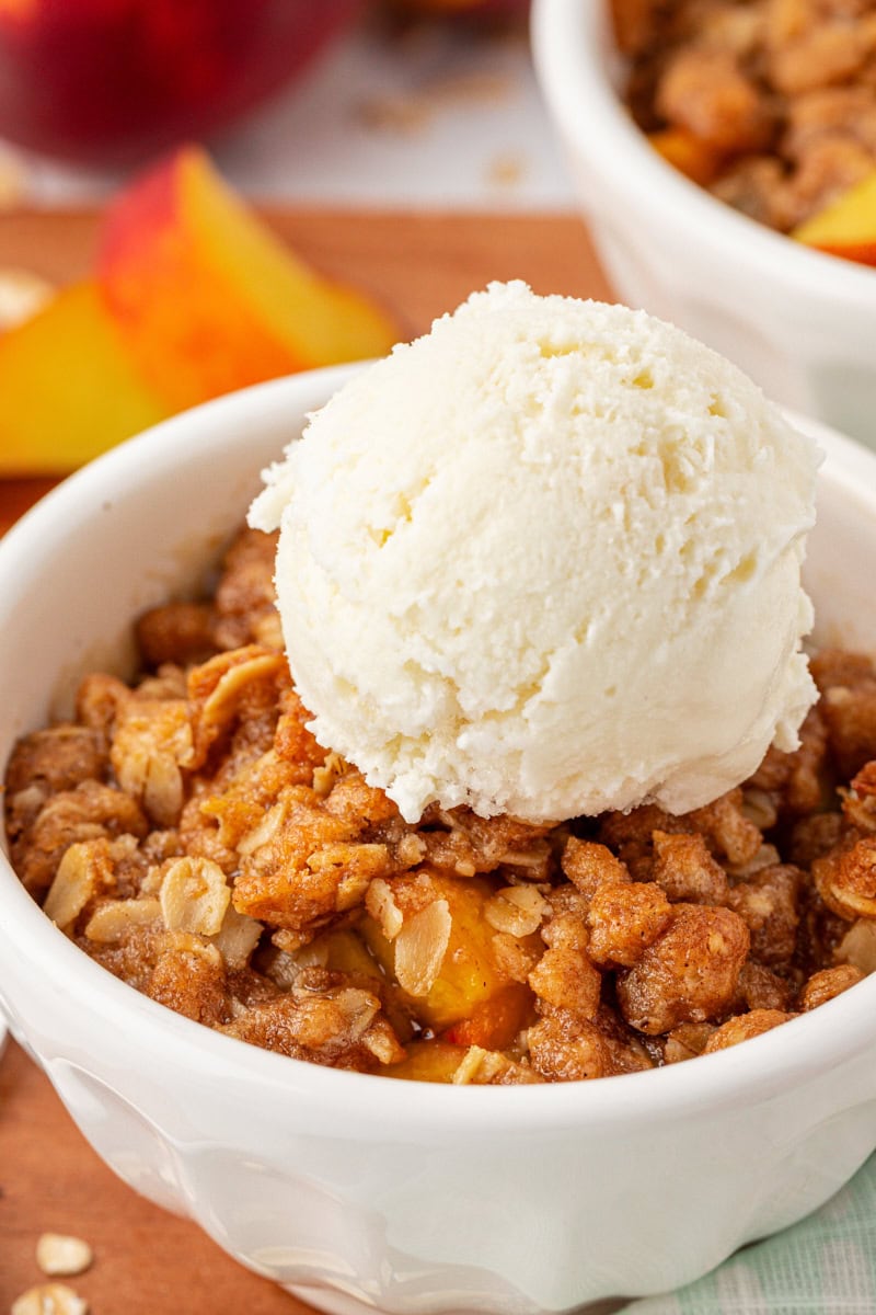 close-up view of a serving of peach crisp topped with ice cream in a white bowl