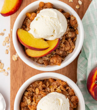 overhead view of peach crisp for two in white bowls set on top of a wooden board