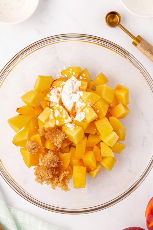 overhead view of peaches, brown sugar, cornstarch, and almond extract in a glass mixing bowl