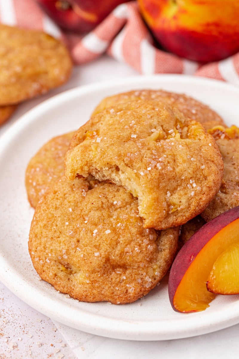 peach cookies on a white plate with more cookies and fresh peaches in the background