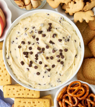overhead view of cookie dough dip in a white bowl with cookies, pretzels, and more dippers surrounding